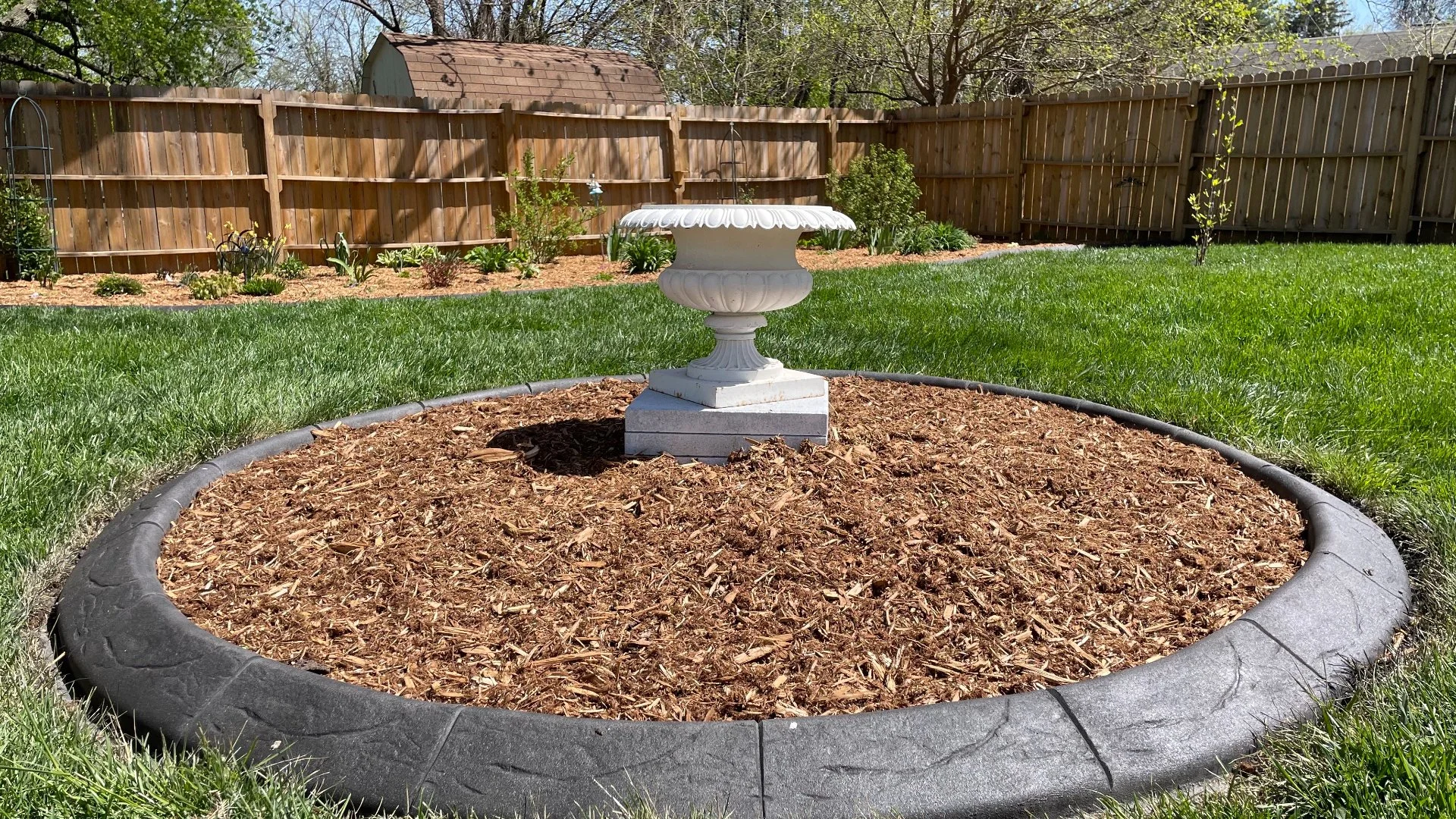 Mulched landscape bed with decorative planter and stamped concrete border.