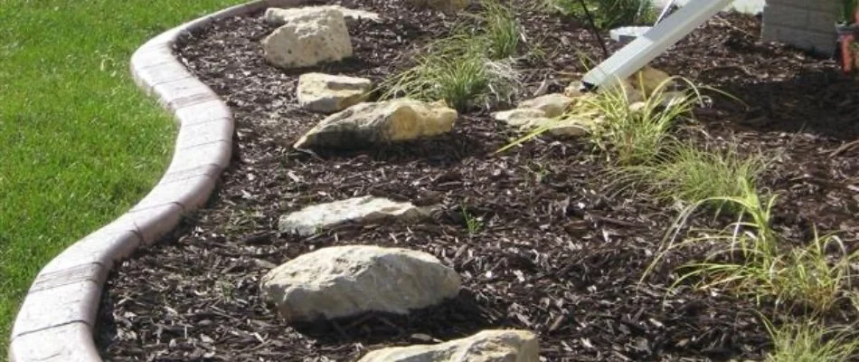 Landscape bed in Des Moines, IA, with mulch, rocks, and concrete edging.