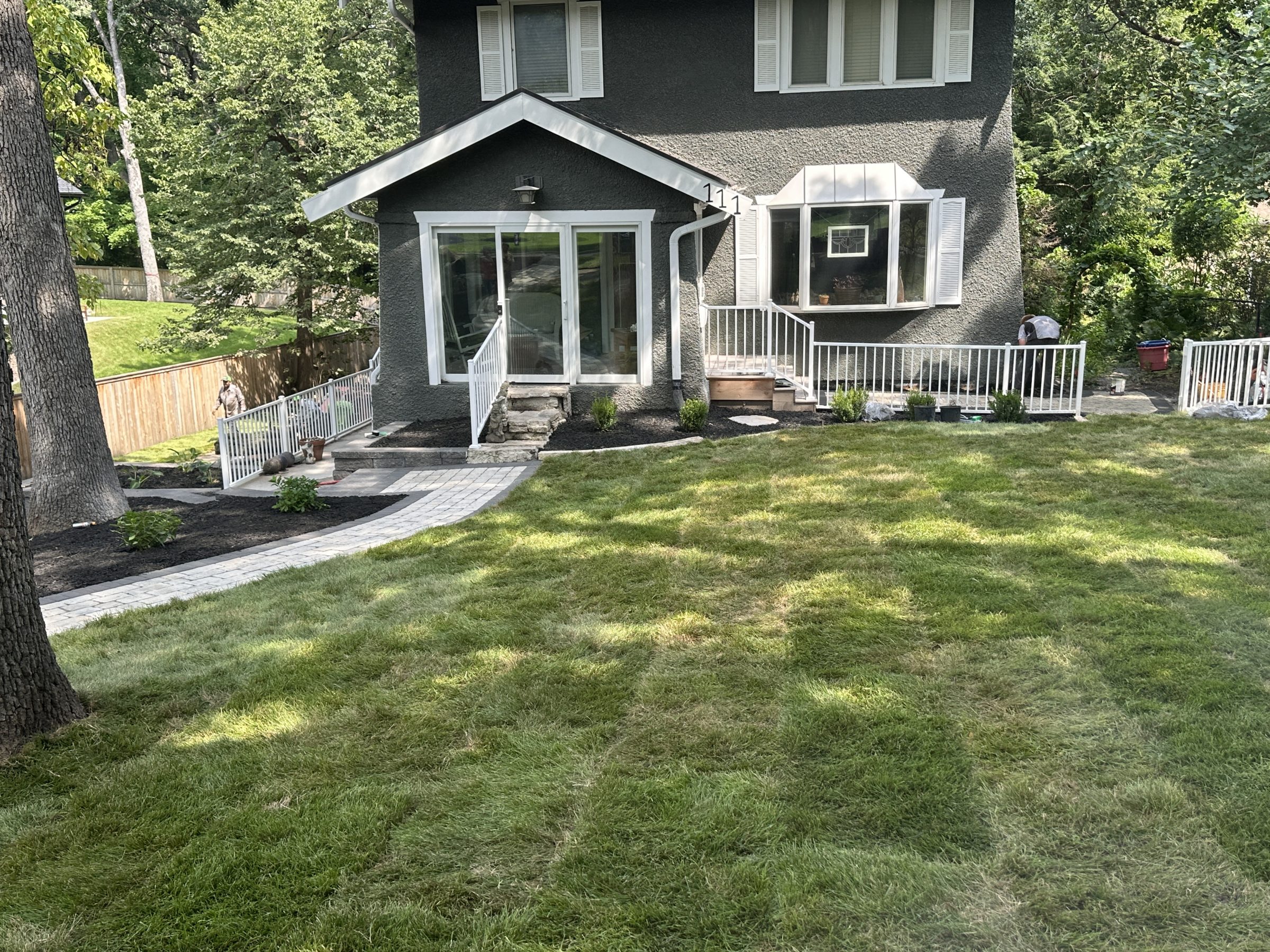 residential landscape showcasing a maintained lawn, walkway, mulch, and fences