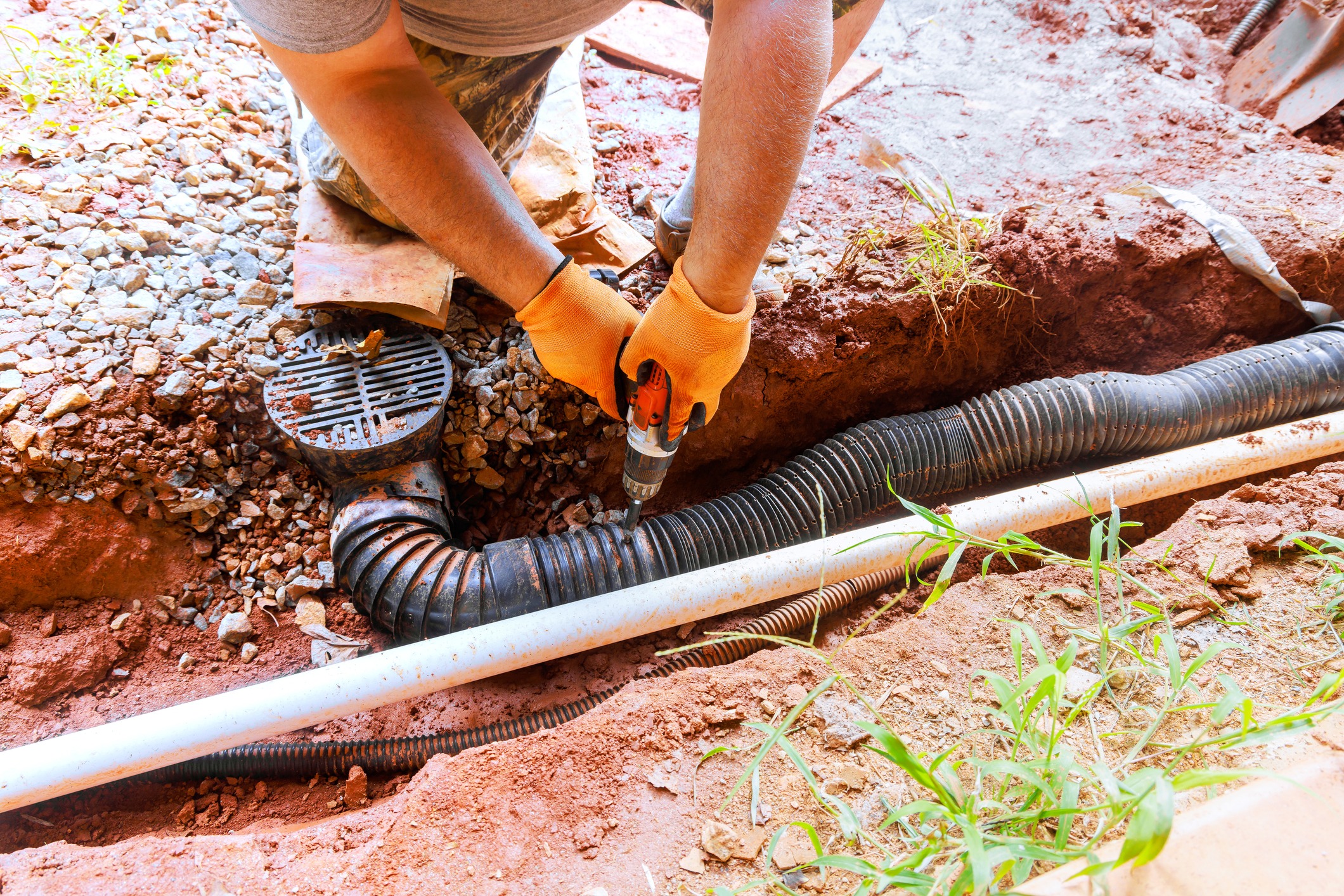 Homeowner performing drainage system repair in residential yard during work day